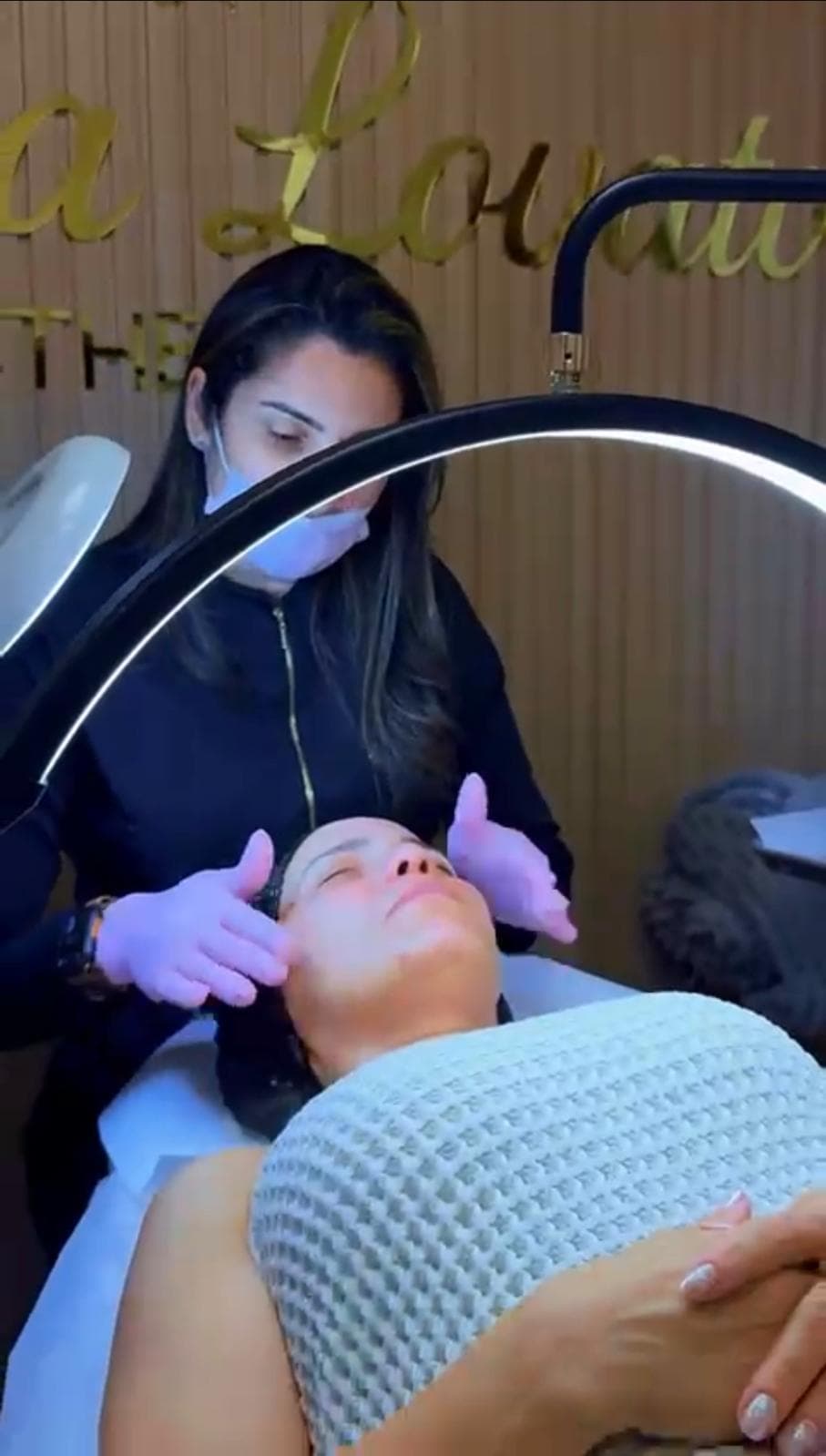 Debora massages a client’s face under a ring light.