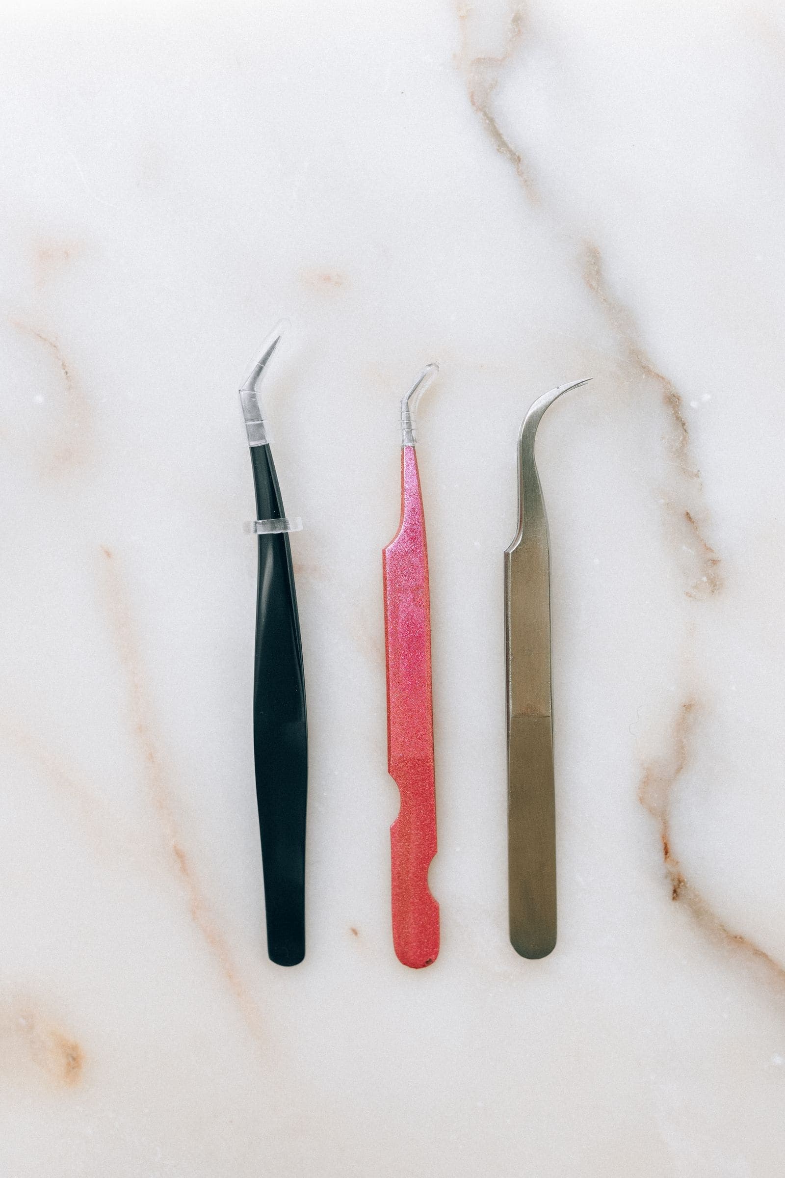 Three pairs of tweezers on a marble surface.