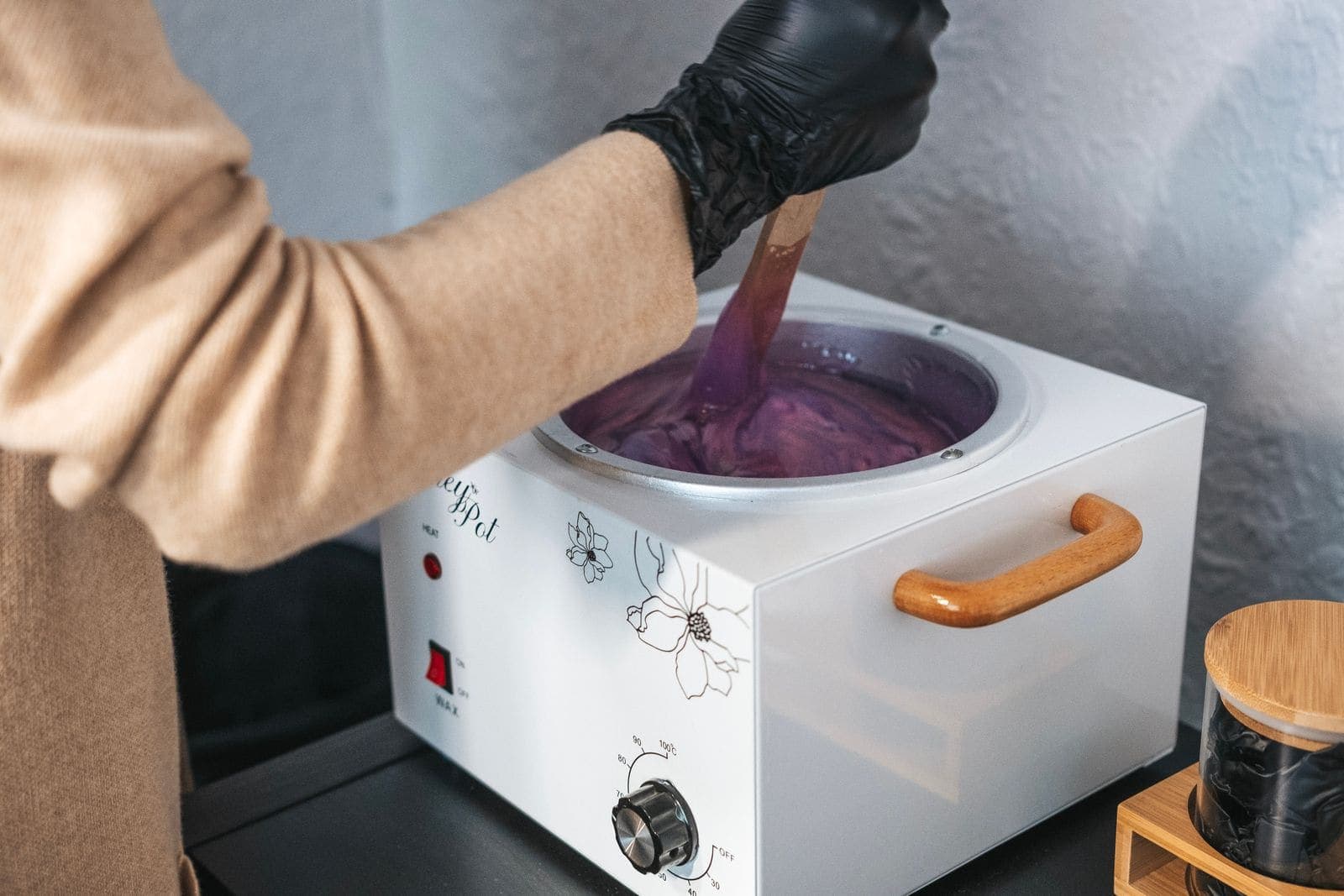 A wax warmer being stirred with a wooden spatula.