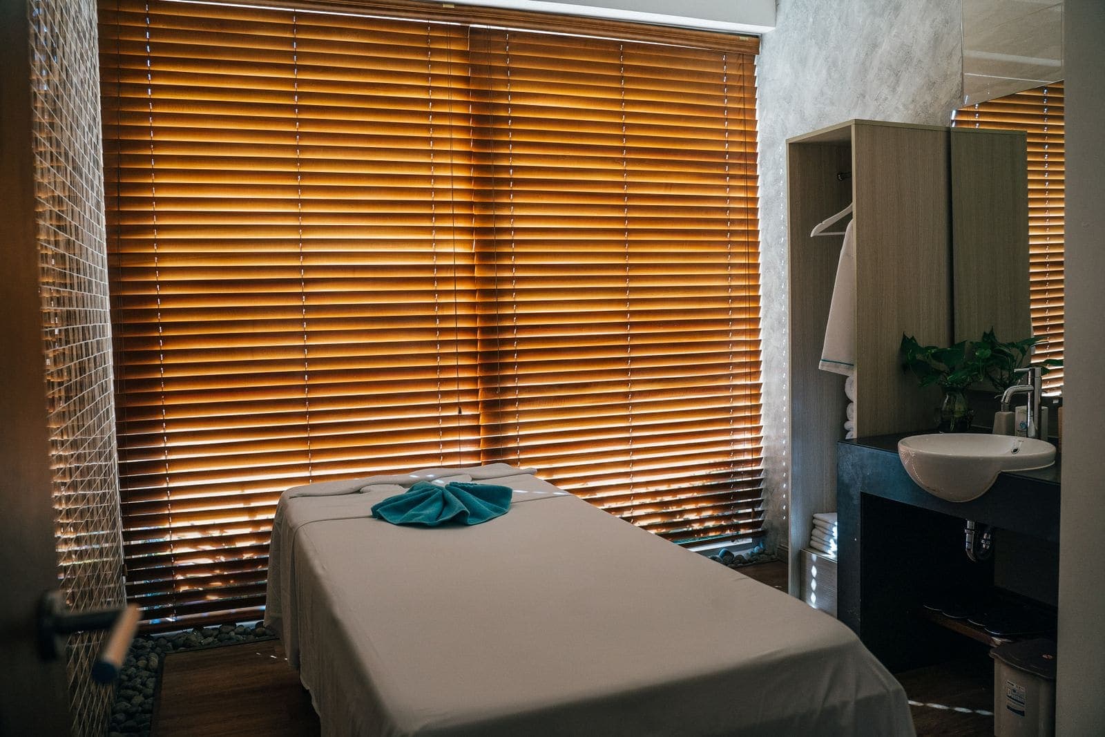 A treatment room with a massage table beside wooden blinds.